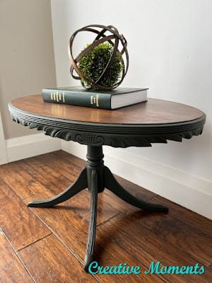 antique tble in green wit a wood top. On otp is a book and orb with a moss ball inside