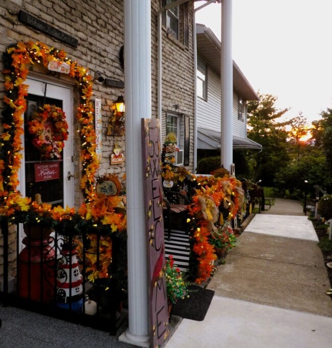 front porch decorated with colorful fall decorations. Including fall leaf garland, wreath on the door and over the sidewalk rail
