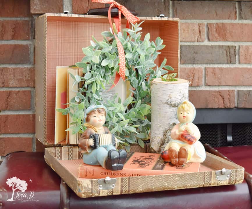 vintage suitcase open with a wreath, books, figurines and a candle sitting inside