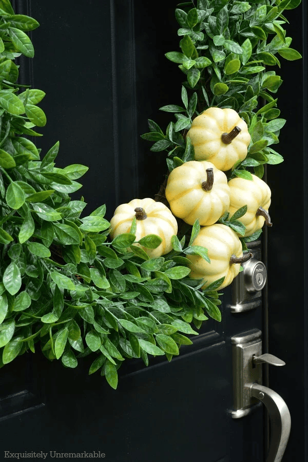 green leaf wreath with small white pumpkins hanging on a black door