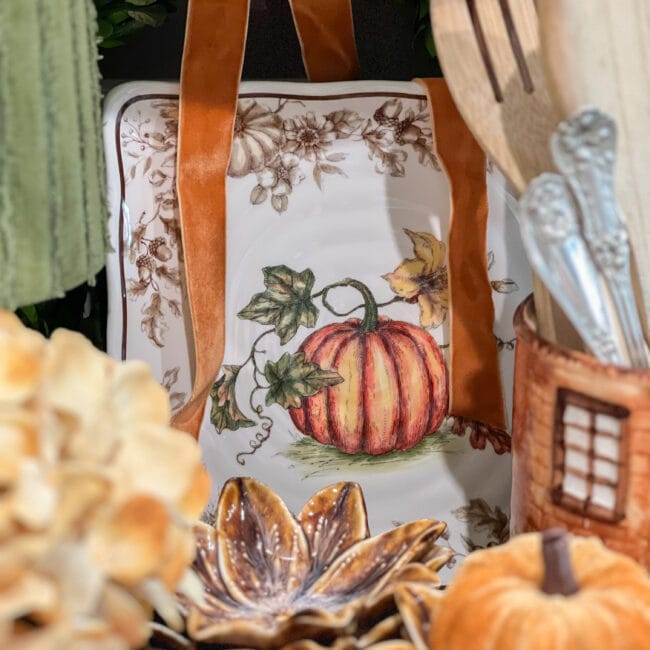 close up of a fall plate with a pumpkin, with a gold hydrangea flower and a cookie jar with wooden spoons