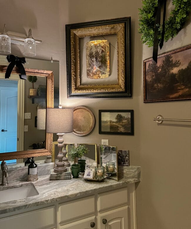 bathroom with wall collage of frames, landscapes, lamp, topiary and silver tray with soaps and a candle