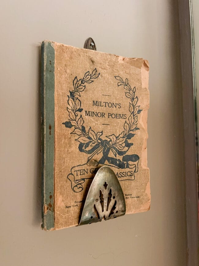 a silver plated cake server bent and hung on the wall as it's holding up a vintage book of poems