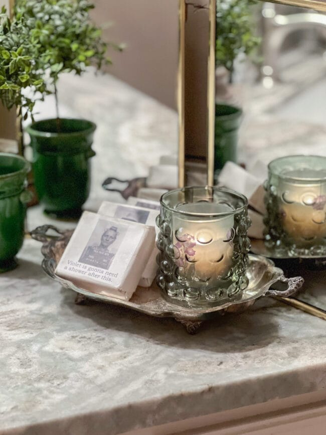small silver tray holding a green glass candle with funny bar soaps