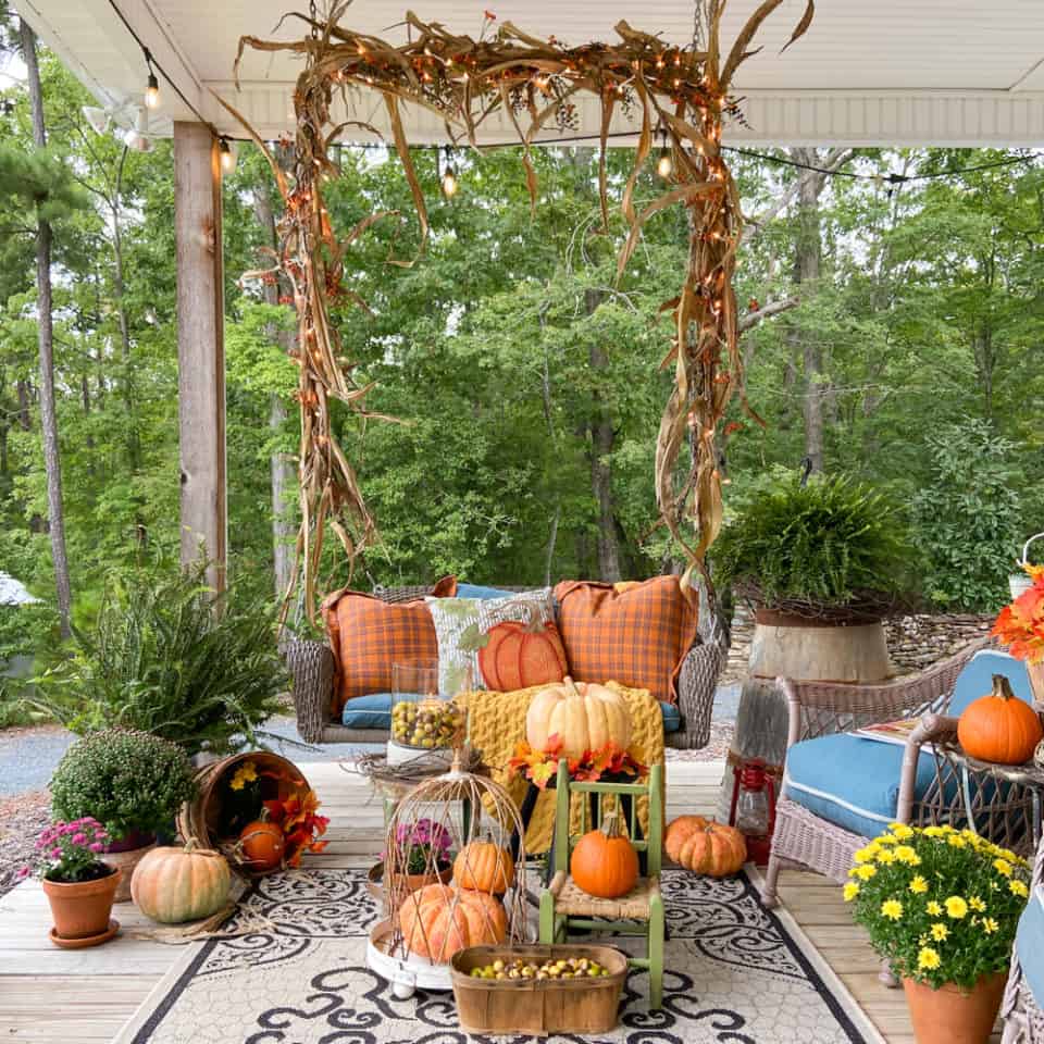fall front porch with a swing, pillows, pumpkins, mums and large ferns