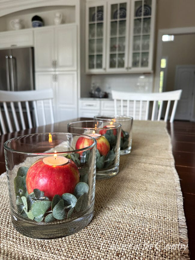 table with red apples and tea lights inside a clear glass vase running down the table