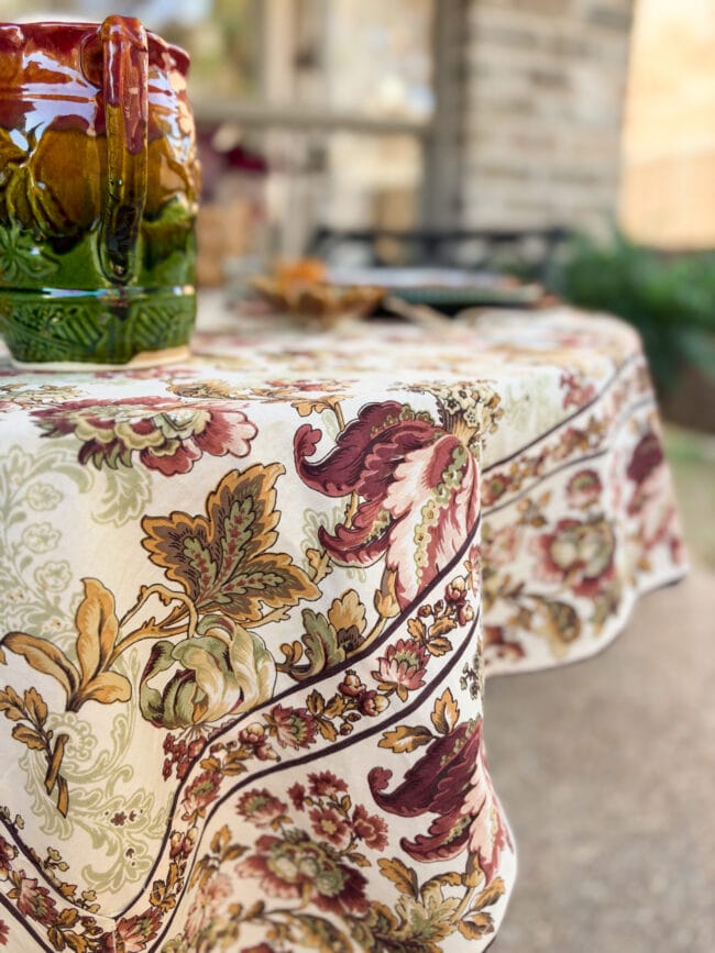 Close up image of the edge of a fall tablecloth with burgundy, gold and soft green color