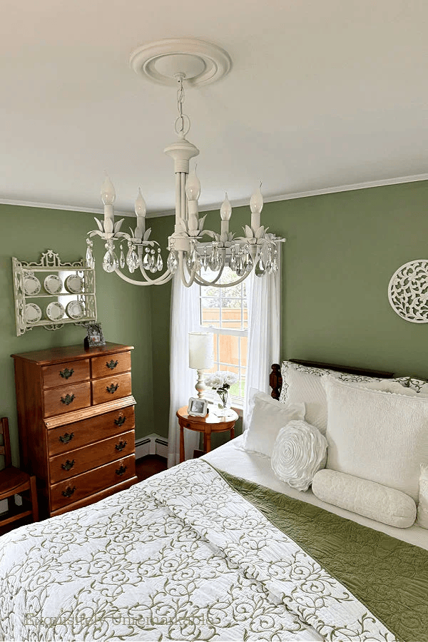 green walls in a bedroom with a green and white quilts, a vintage chest of drawers and a white chandelier